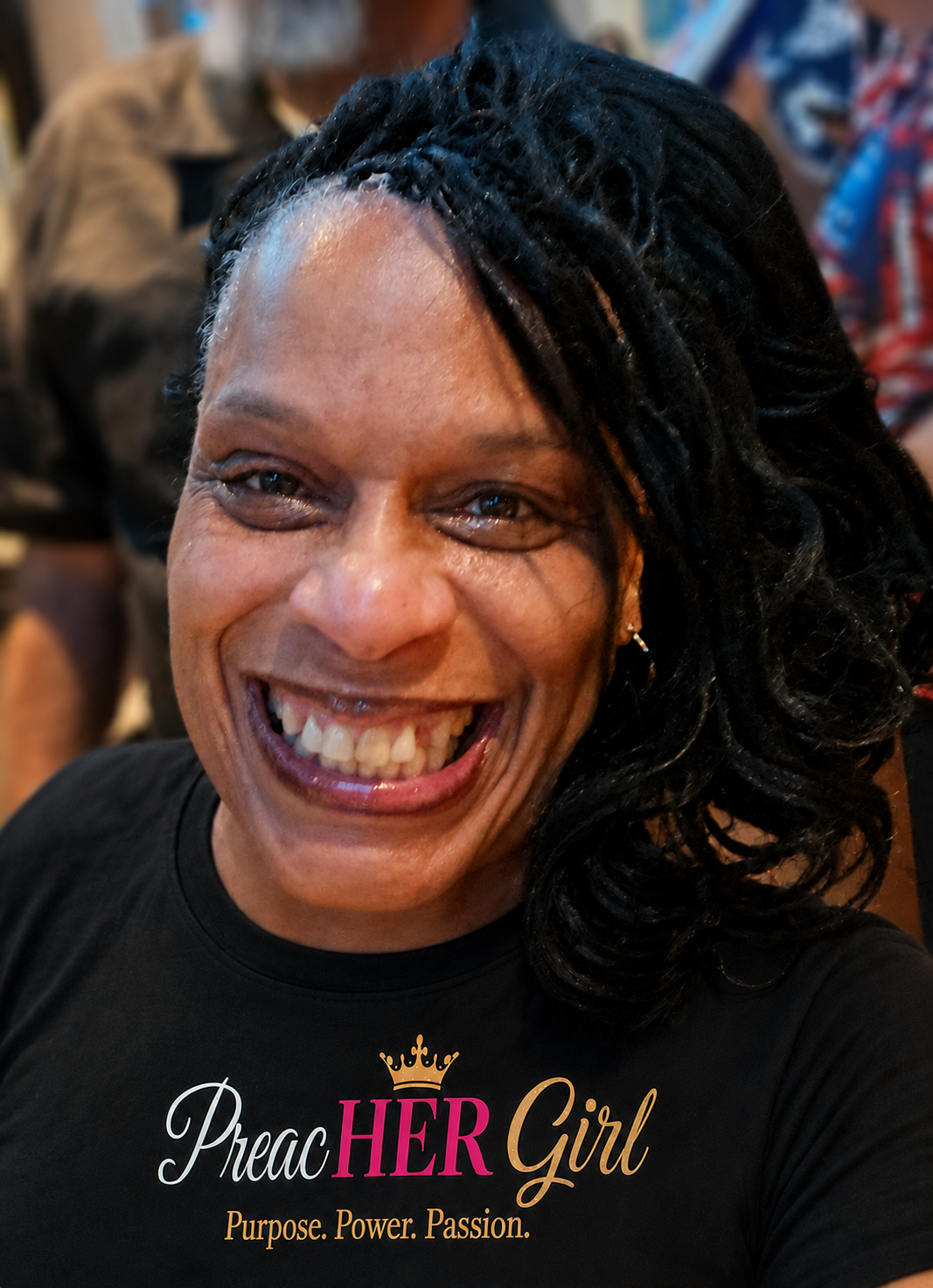Michell A. Jackson smiling in a black PreacHER Girl shirt with a gold crown over fuchsia HER and the words Purpose. Power. Passion., photographed against a softly blurred background.